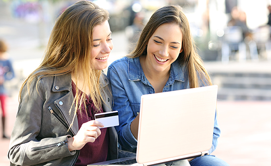 Two young women buying online with credit card, financial education